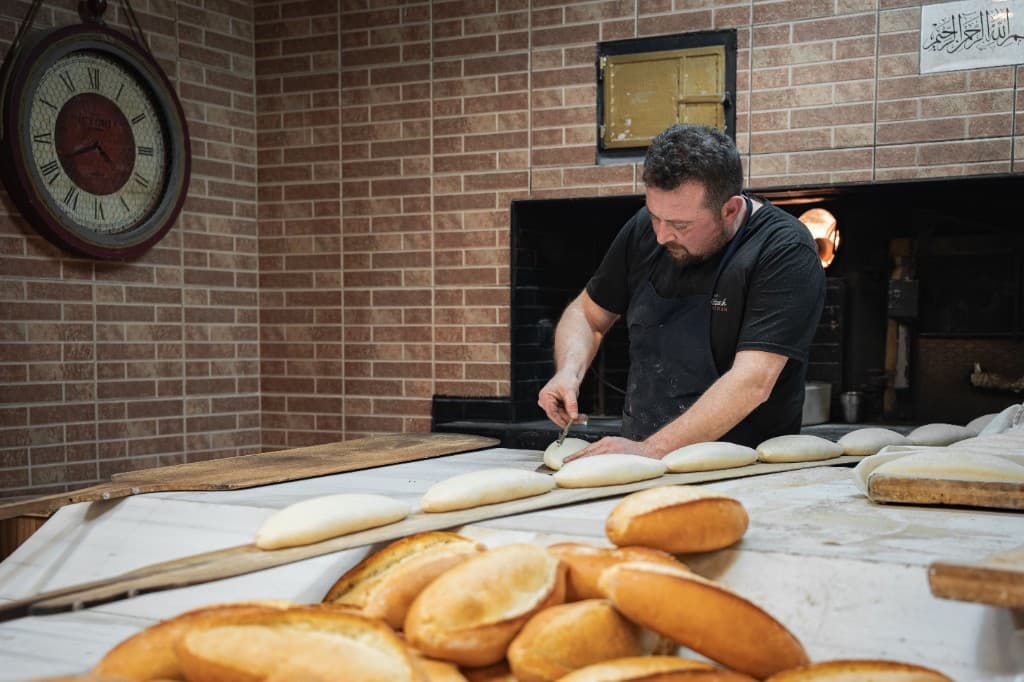 Bakker aan het werk: broodjes snijden en verse bollerig brood in de bakkerij